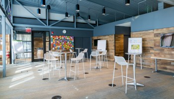 A modern classroom with high ceilings, chairs, desks, whiteboards, and colorful sticky notes on the back wall.