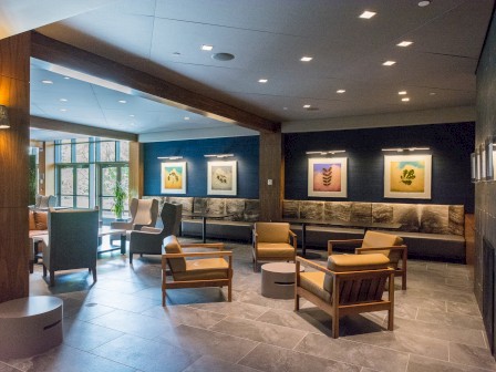 The image depicts a modern lobby or lounge area with comfortable seating, art on the walls, and large windows letting in natural light.