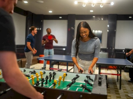 People are enjoying foosball and table tennis in a recreational room, having fun in a lively social setting.