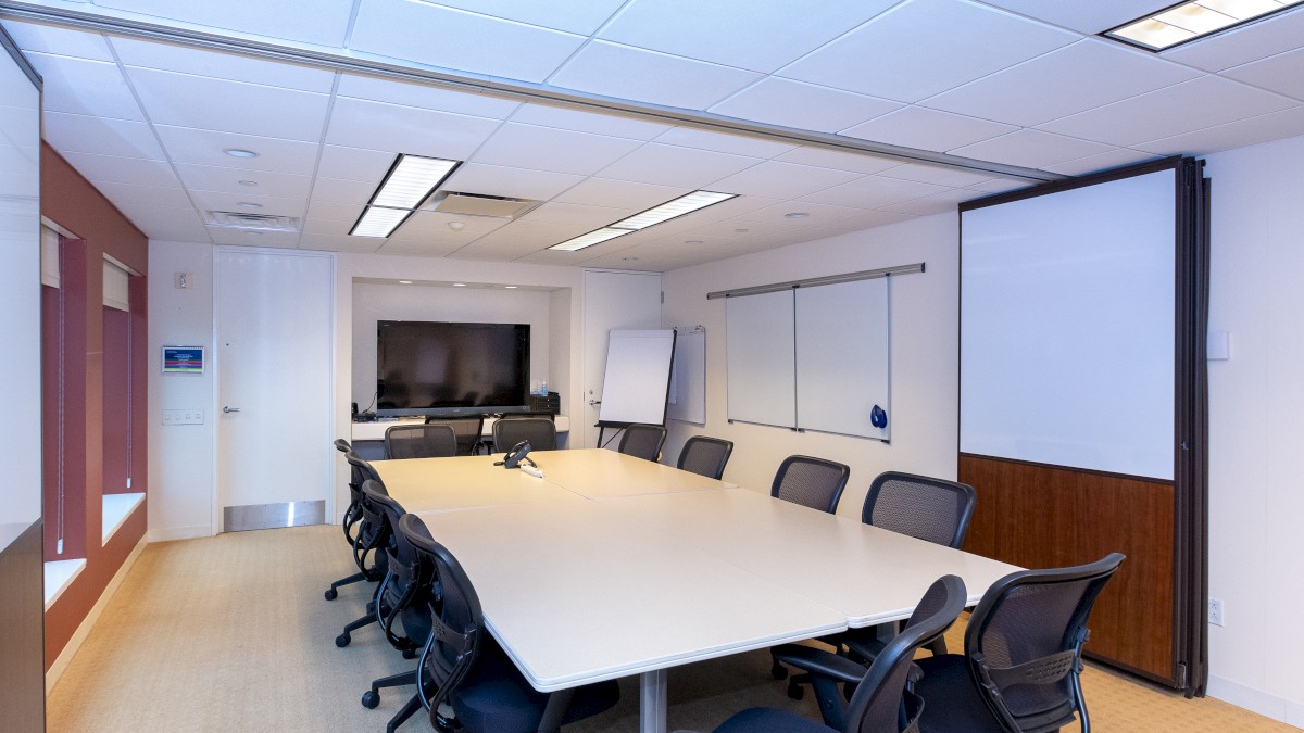 A modern conference room with a long table, several office chairs, a large wall-mounted TV, a whiteboard, and a flip chart stand ends the sentence.