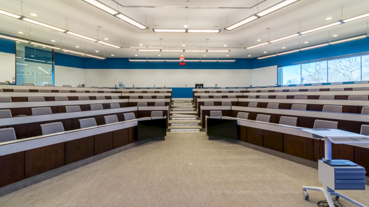 The image shows a modern lecture hall with tiered seating, a podium, and wide windows, designed for academic presentations or conferences.