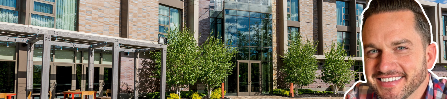 The image features a modern building with large windows and a courtyard, alongside an added picture of a man smiling in the lower right corner.