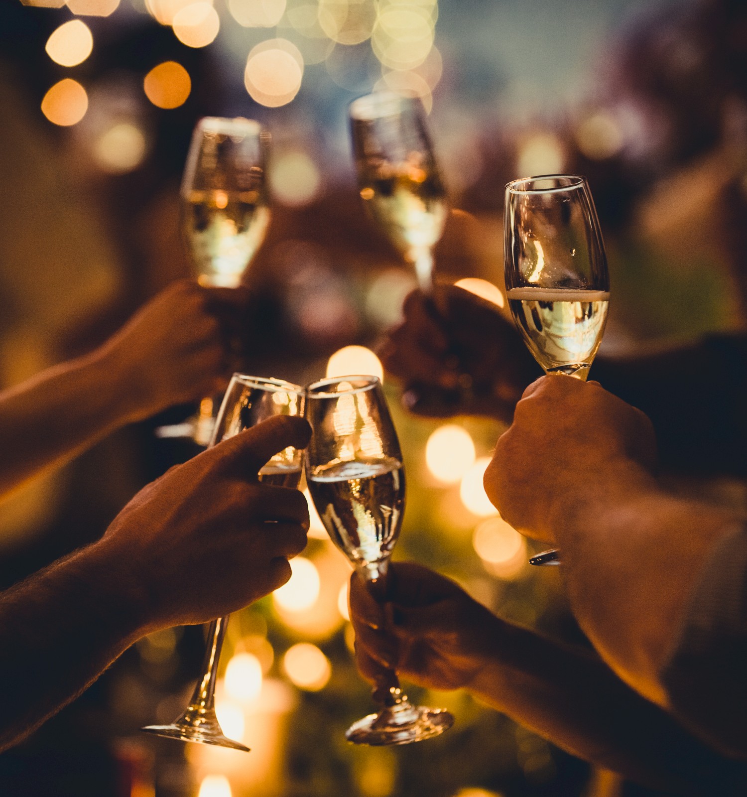 People are raising champagne glasses in a toast at a celebration, with warm, festive lighting and bokeh effects in the background.