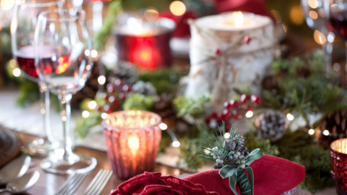 A festive holiday table setting with red napkins, wine glasses, candles, and greenery, creating a cozy and elegant atmosphere.