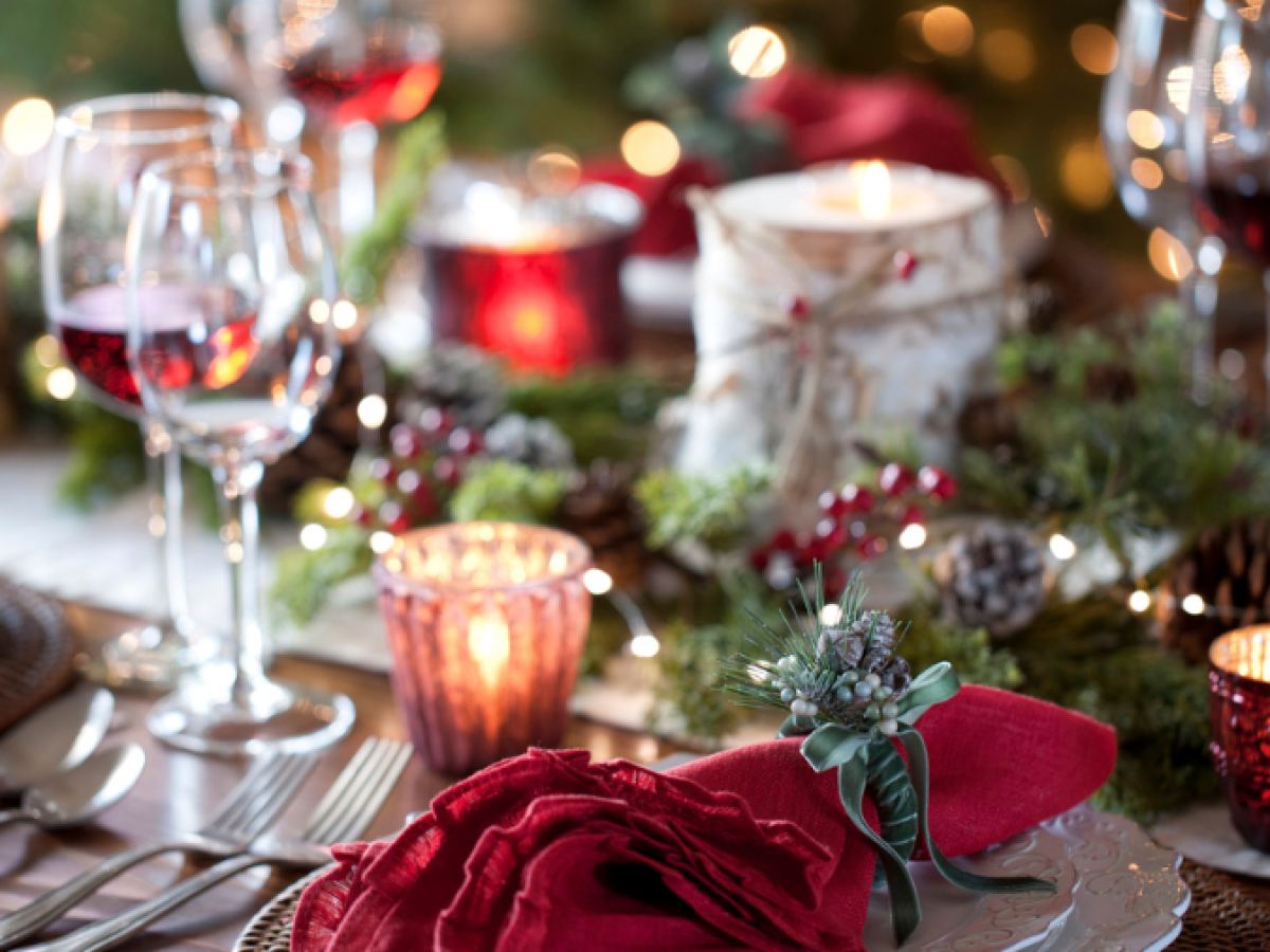 A festive holiday table setting with red napkins, wine glasses, candles, and greenery, creating a cozy and elegant atmosphere.