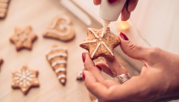 A person is decorating star-shaped cookies with white icing, using a piping bag. Various decorated cookies are visible on the table.